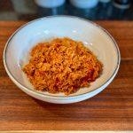 Bowl on a wooden board containing Mexican style tomato rice. Fresh tomatoes in the rice
