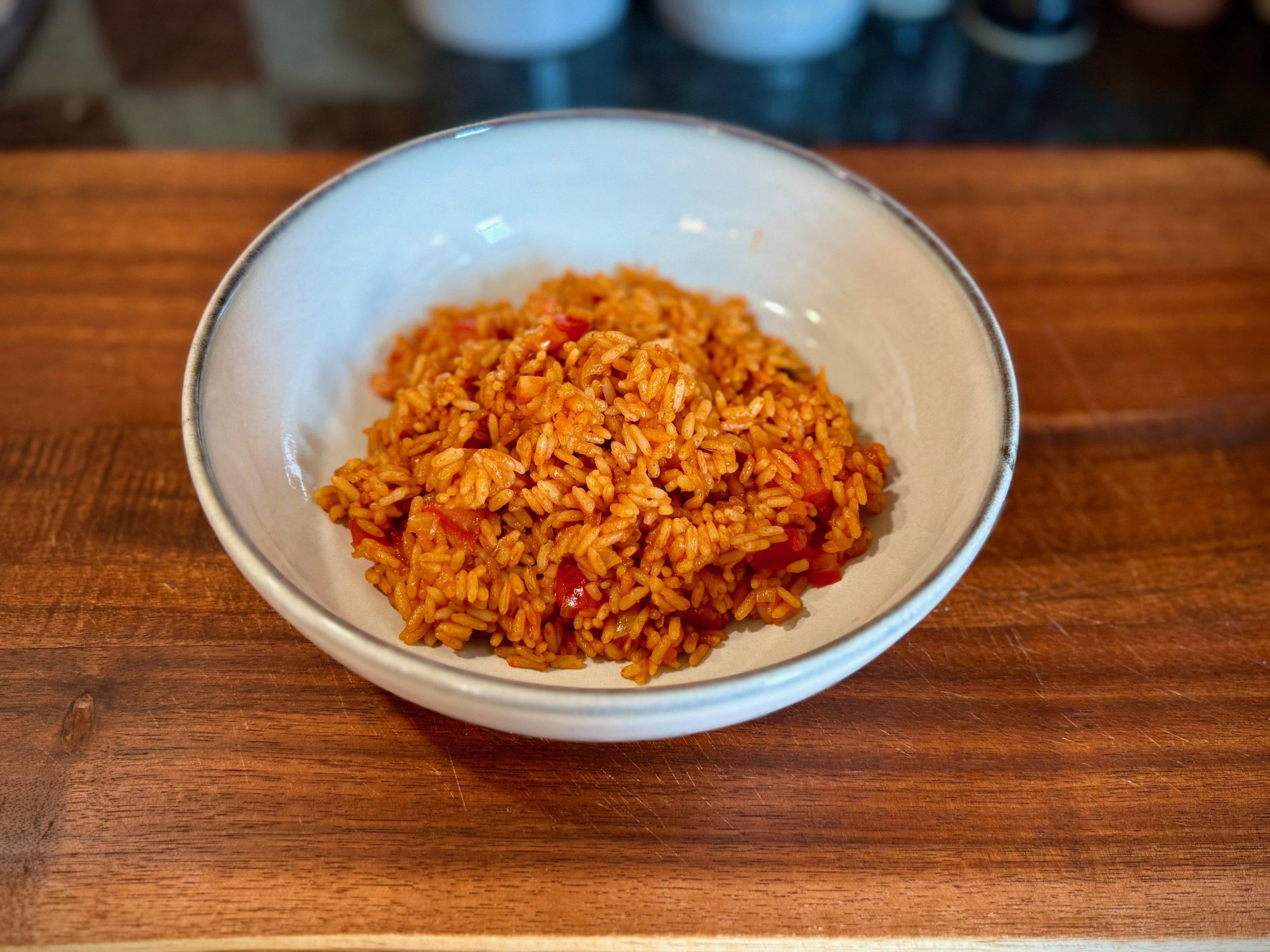 Bowl on a wooden board containing Mexican style tomato rice. Fresh tomatoes in the rice