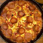 Cast iron pan on wooden board with a crispy, fluffy pepperoni pan pizza in it.