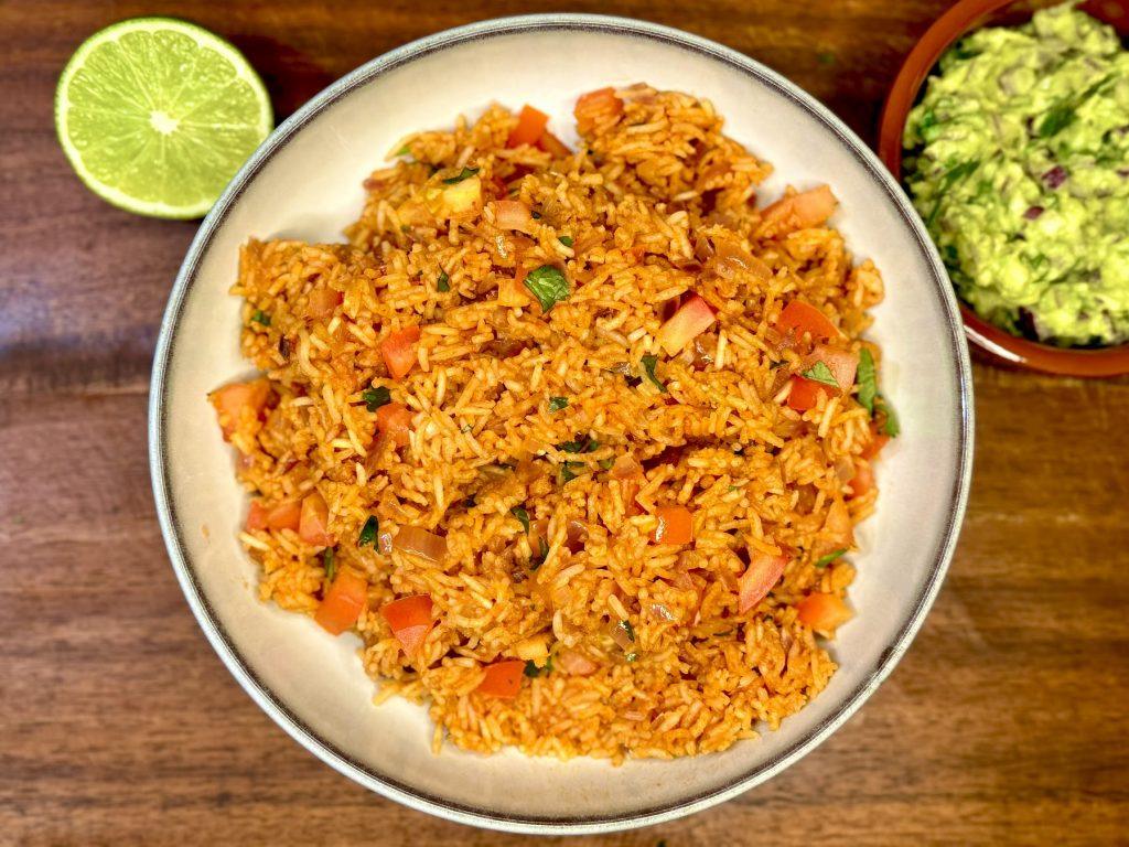 Bowl on a wooden board containing Mexican style tomato rice. Fresh tomatoes in the rice