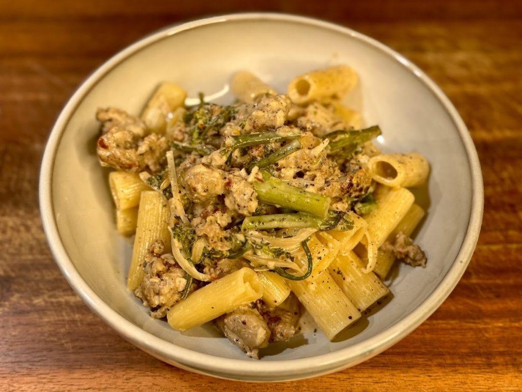 Bowl of pasta with sausage and broccolini with a creamy sauce.