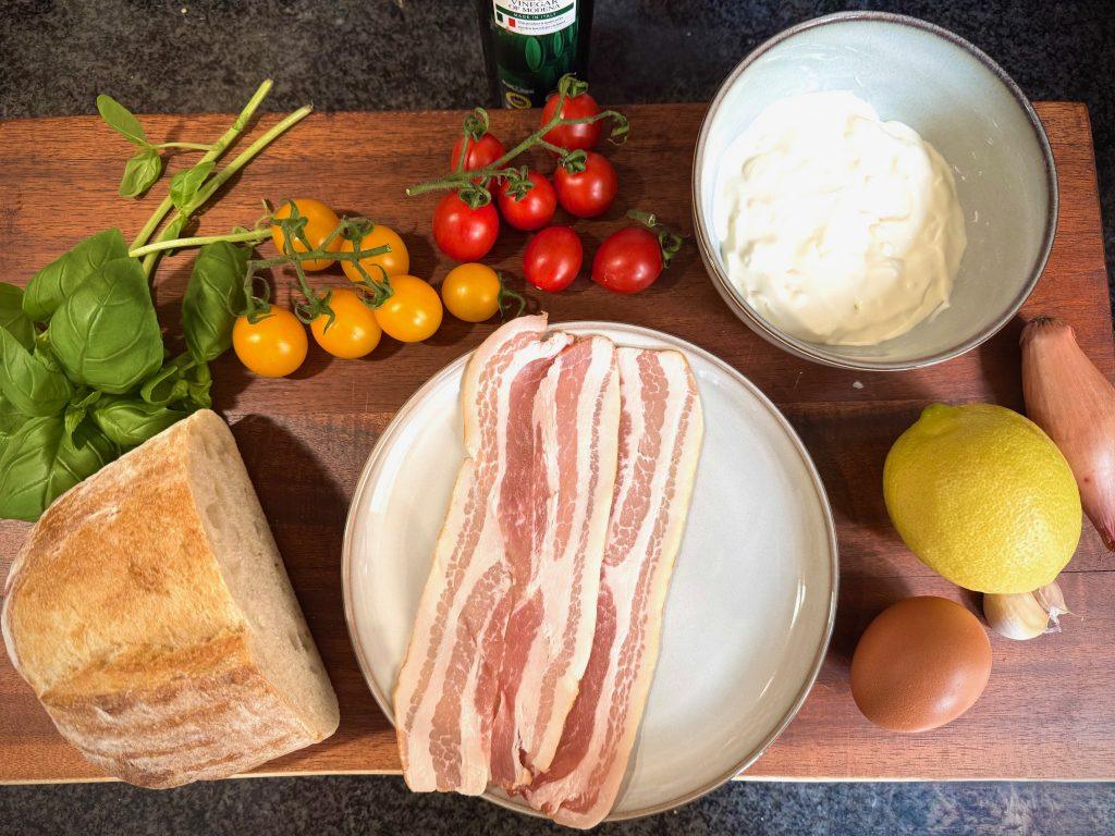 Tomatoes, lemon, shallots, ricotta, bacon, basil and sourdough bread on wooden chopping board.