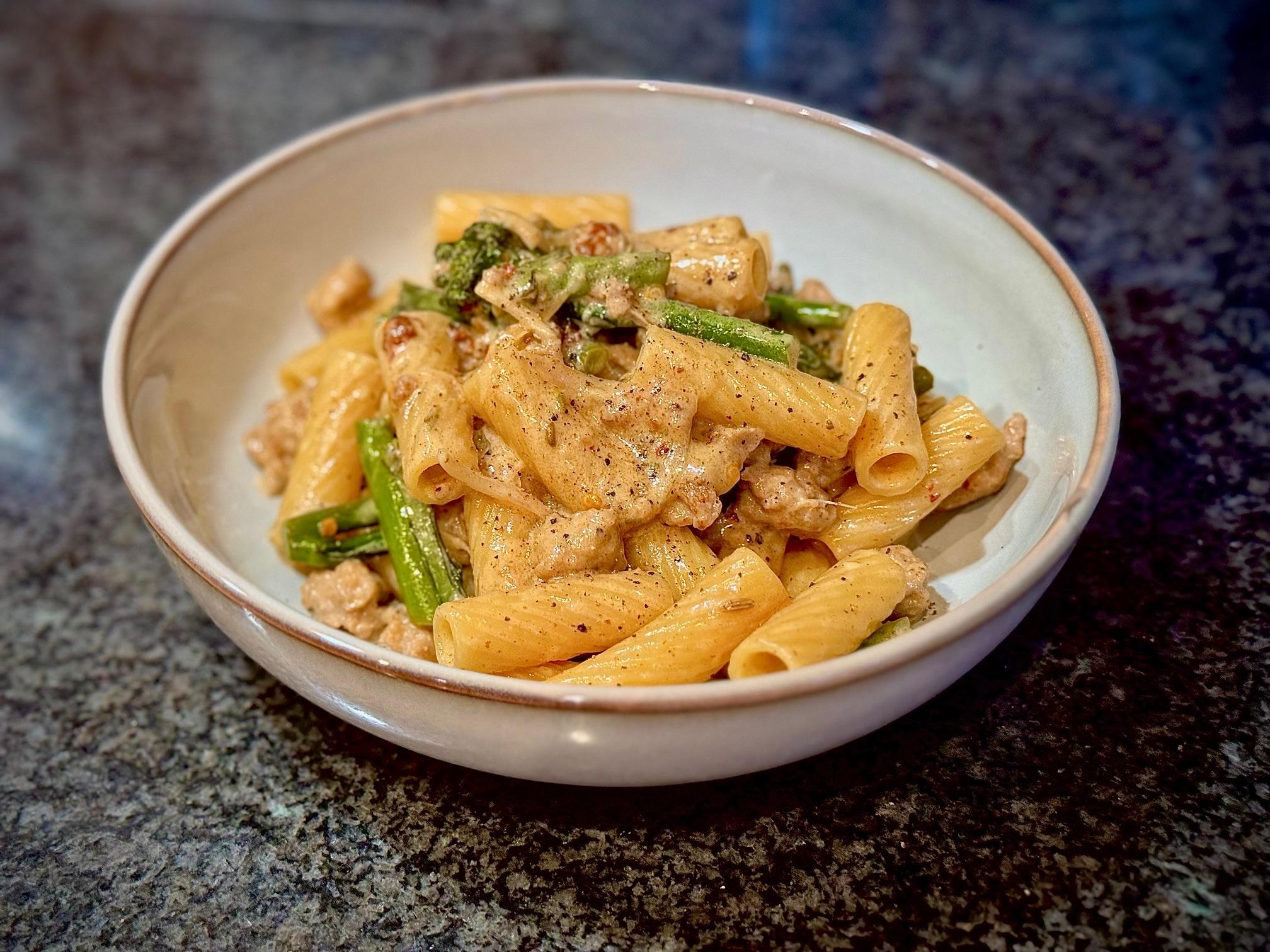 Bowl of pasta with sausage and broccolini with a creamy sauce.