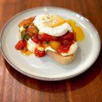 Plate with sourdough toast, whipped ricotta, tomatoes and poached egg on top.