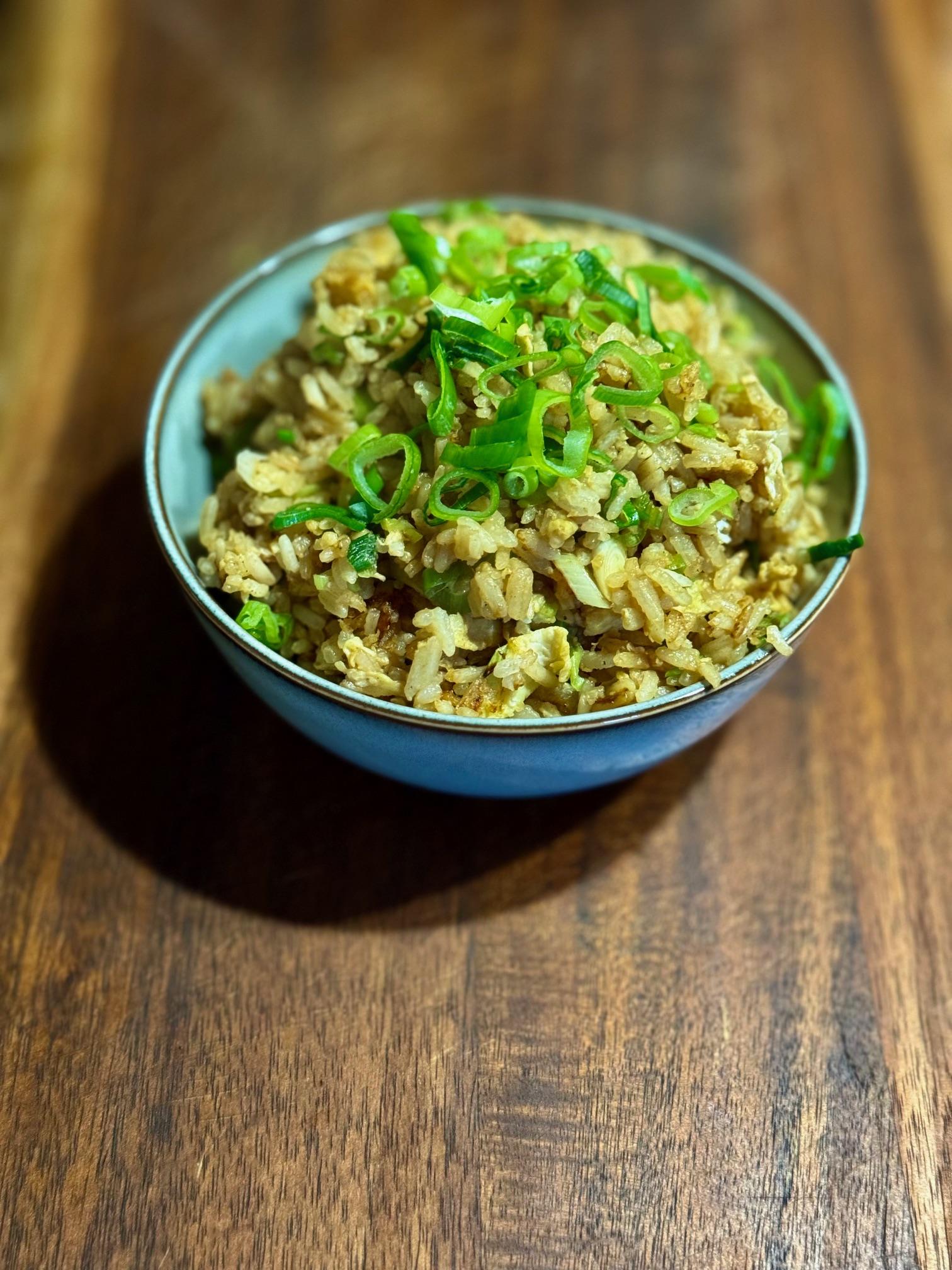 Bowl containing homemade egg fried rice. Topped with sliced spring onions.