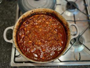 Enamelled cast iron Le Creuset pot on the hob containing slow cooked beef shin chilli.