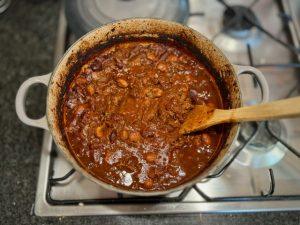 Enamelled cast iron Le Creuset pot on the hob containing slow cooked beef shin chilli.