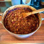 Enamelled cast iron Le Creuset pot onwooden board containing slow cooked beef shin chilli.