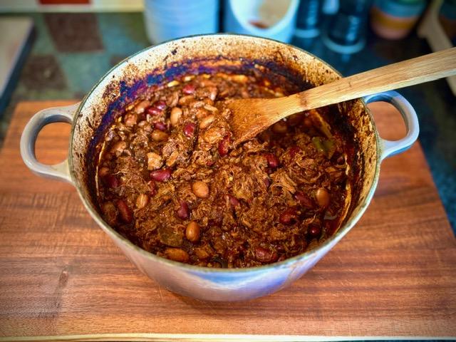 Enamelled cast iron Le Creuset pot onwooden board containing slow cooked beef shin chilli.