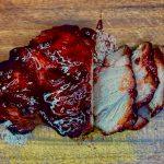 Red, sticky and glazed char siu pork sliced on a wooden chopping board