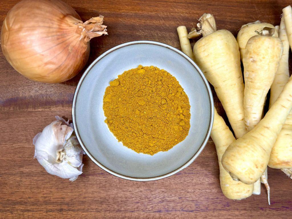 Onion, garlic, parsnips and curry powder on a wooden background.