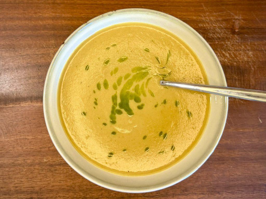 Bowl of curried parsnip soup with coriander oil on a wooden board.