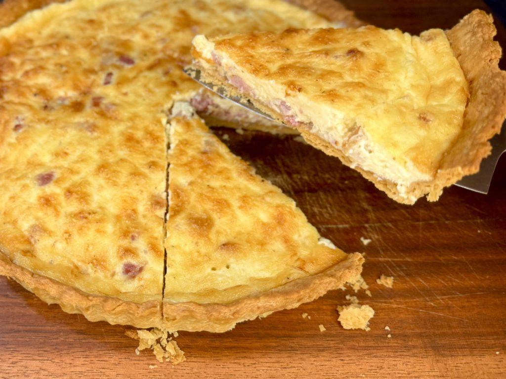 Slice of quiche lorraine being lifted from the quiche.