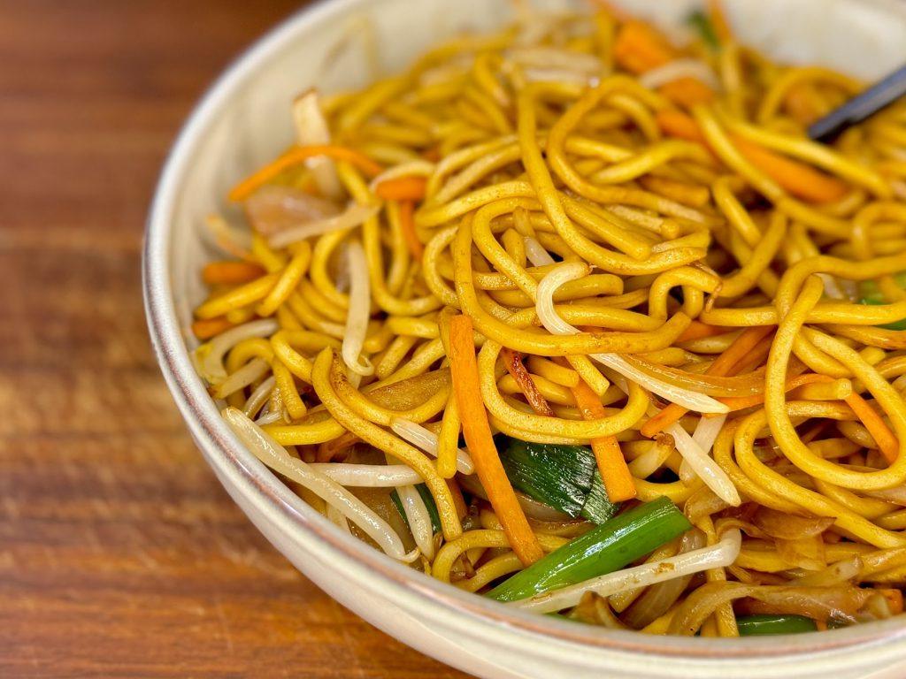 Closeup of a bowl of Chow Mein noodles on a wooden board.