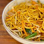 Closeup of a bowl of Chow Mein noodles on a wooden board.