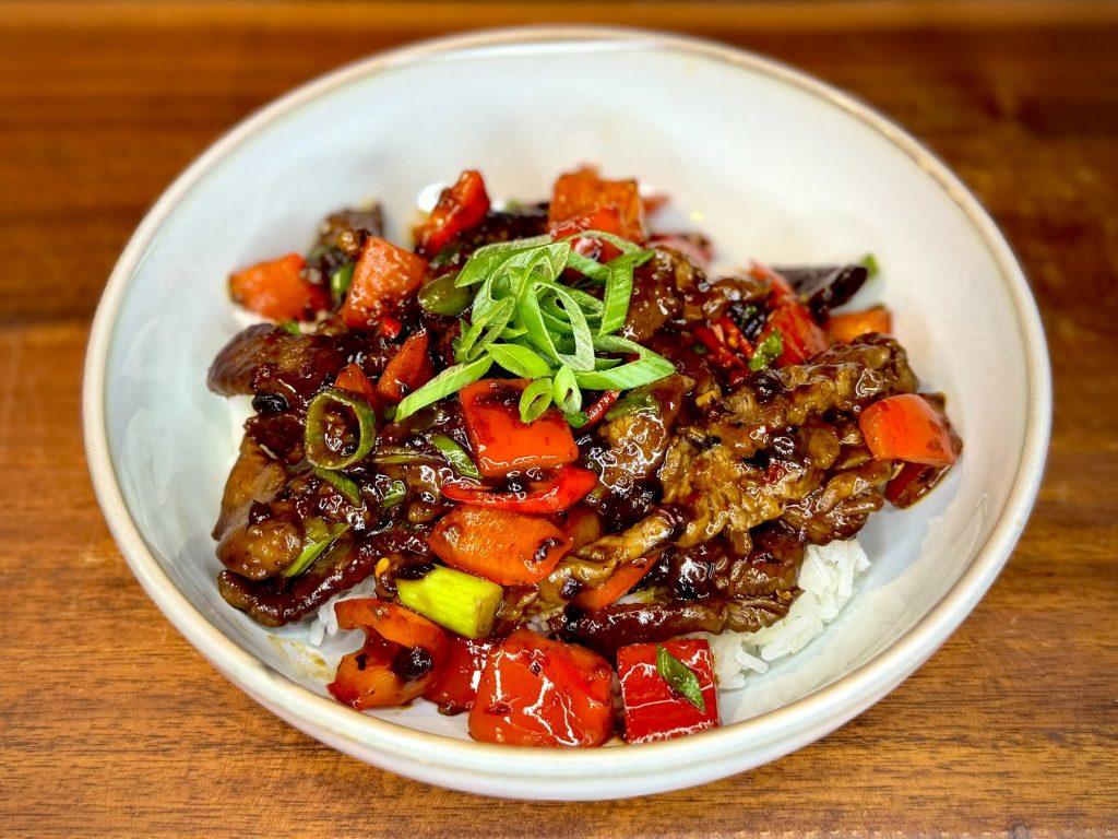 Bowl of Hunan Beef on a wooden board.