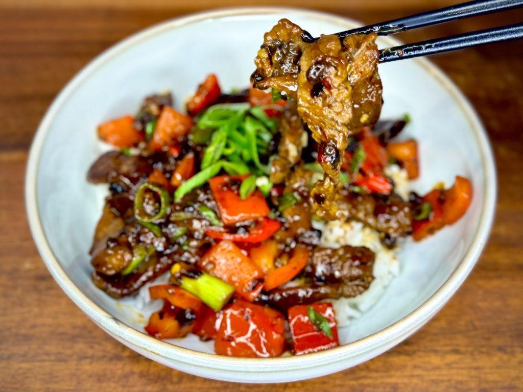 Bowl of Hunan Beef on a wooden board.