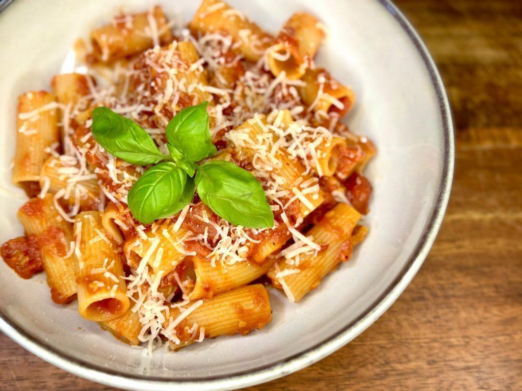 Bowl of pasta all'arrabbiata in a bowl with parmesan cheese and basil leaves.