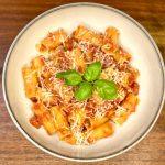Bowl of pasta all'arrabbiata in a bowl with parmesan cheese and basil leaves.