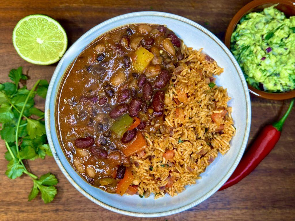 Bowl of three bean chilli and rice, alongside some coriander and a lime.