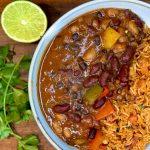 Bowl of three bean chilli and rice, alongside some coriander and a lime.