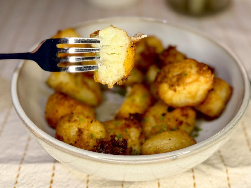 Close up of a potato from a bowl of roast potatoes with rosemary garlic salt.