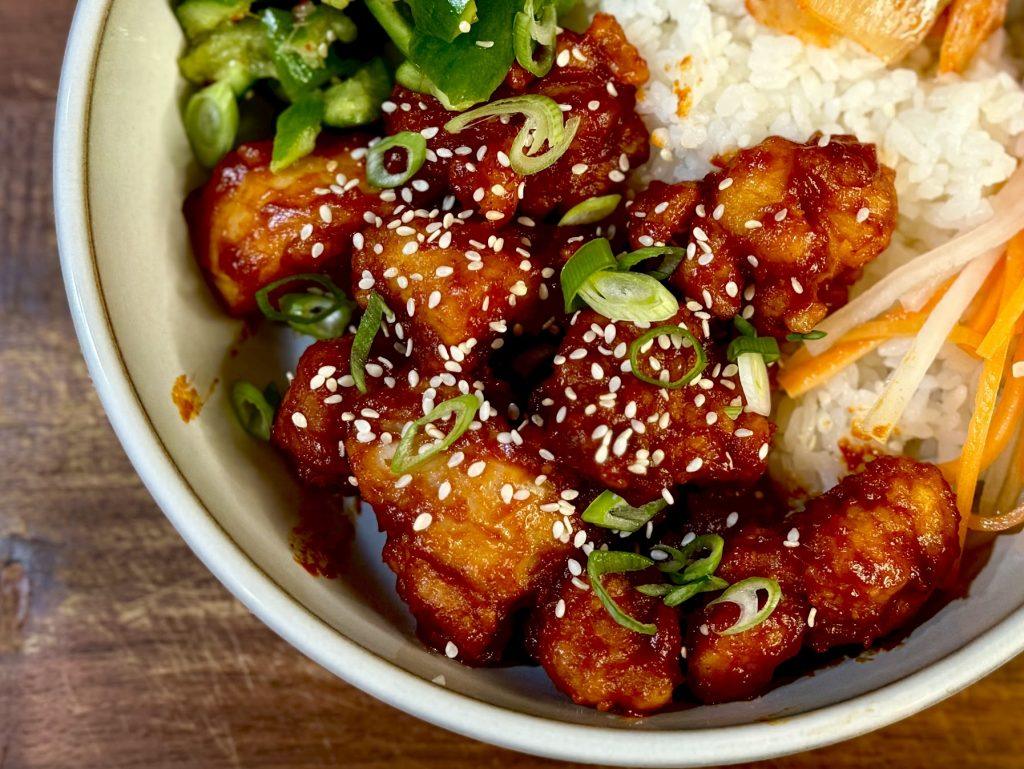 Bowl of crispy korean fried chicken, rice, kimchi, pickles and cucumber with chopsticks