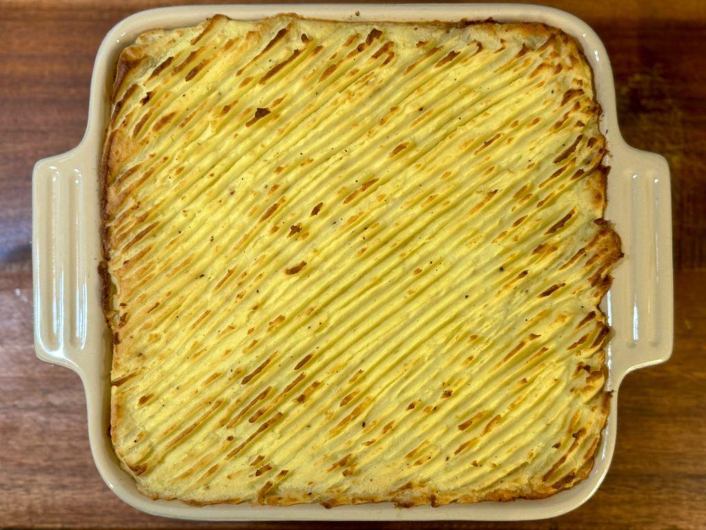 A dish of cottage pie on a wooden surface