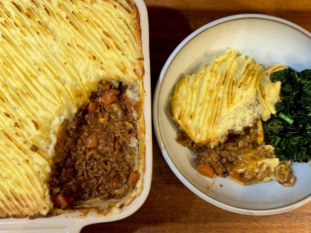 A dish of cottage pie next to a bowl of cottage pie and kale.