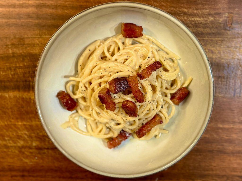 A bowl of spaghetti carbonara on a wooden board.