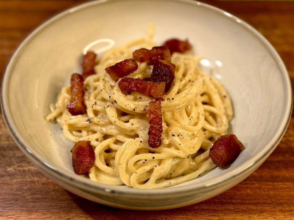 A bowl of spaghetti carbonara on a wooden board.
