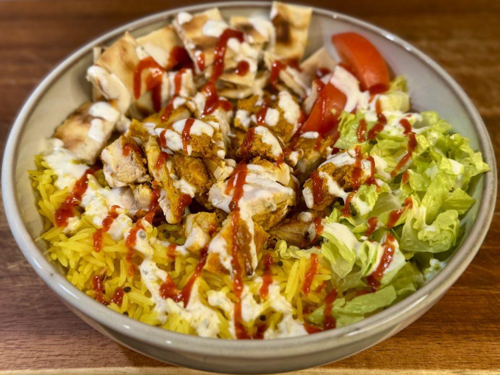 Bowl of halal cart chicken, pilau rice, salad, garlic sauce and chilli sauce.